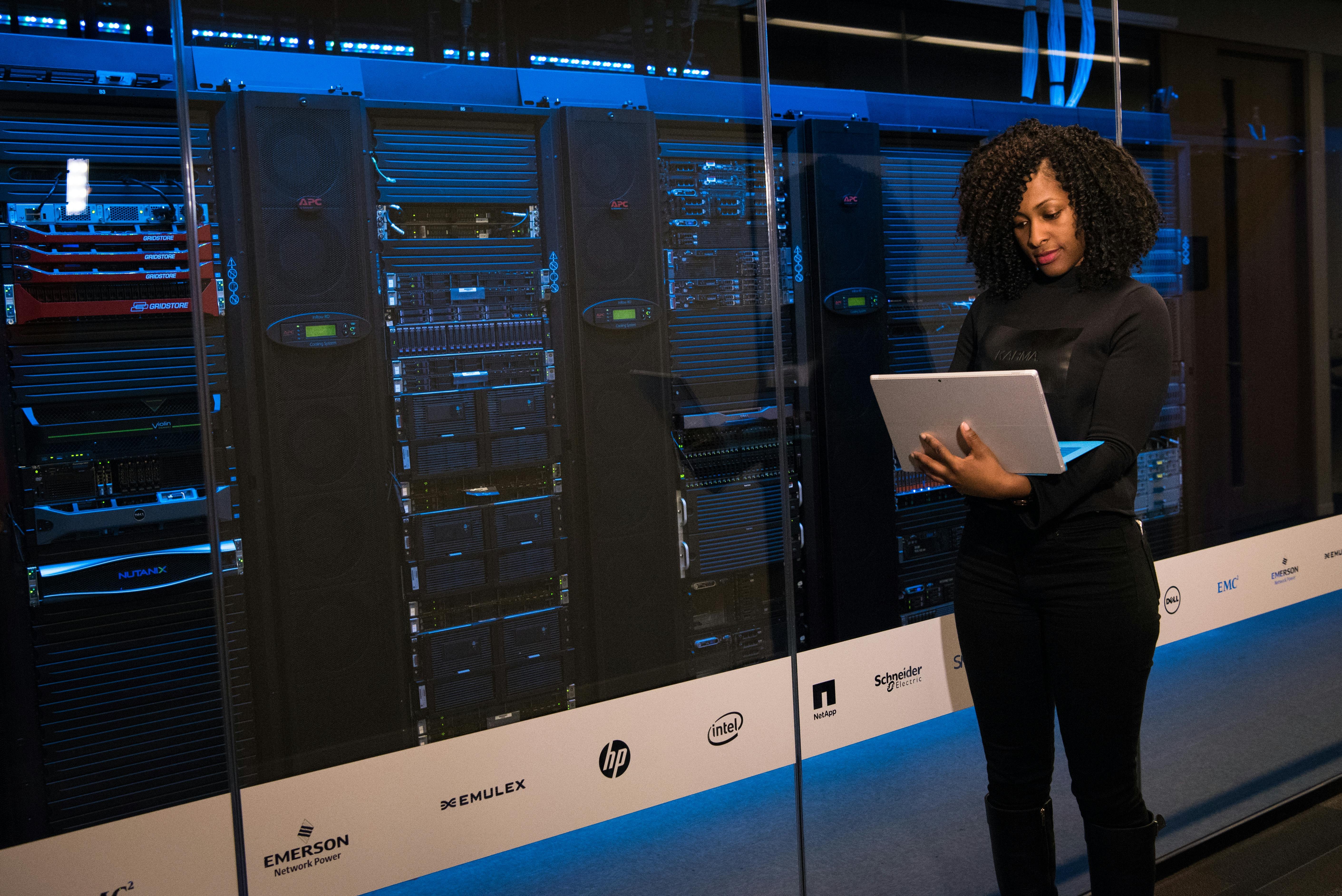 a person standing in front of a rack of servers, examining her laptop